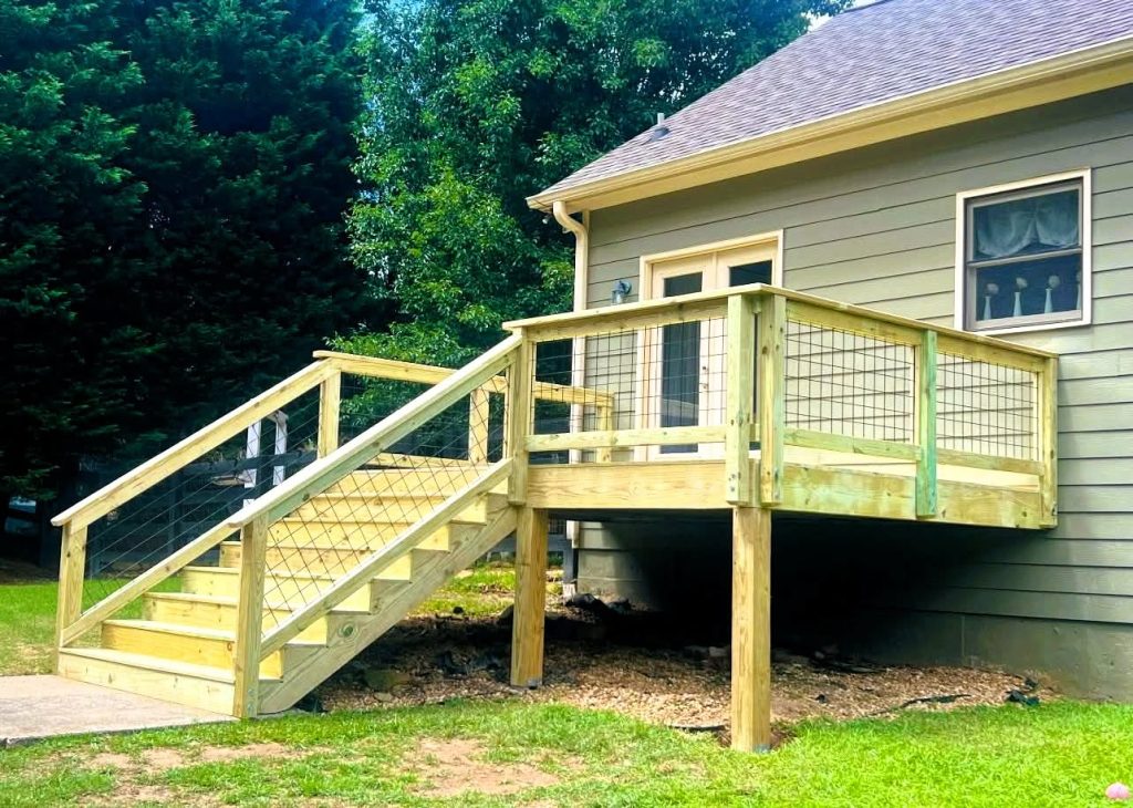 Newly built pressure-treated deck with wire mesh infill railing and a stair run descending to a concrete pad