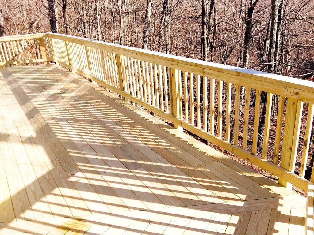 Freshly built pressure-treated deck with an angled bay corner and closely spaced wood baluster railing above winter woods
