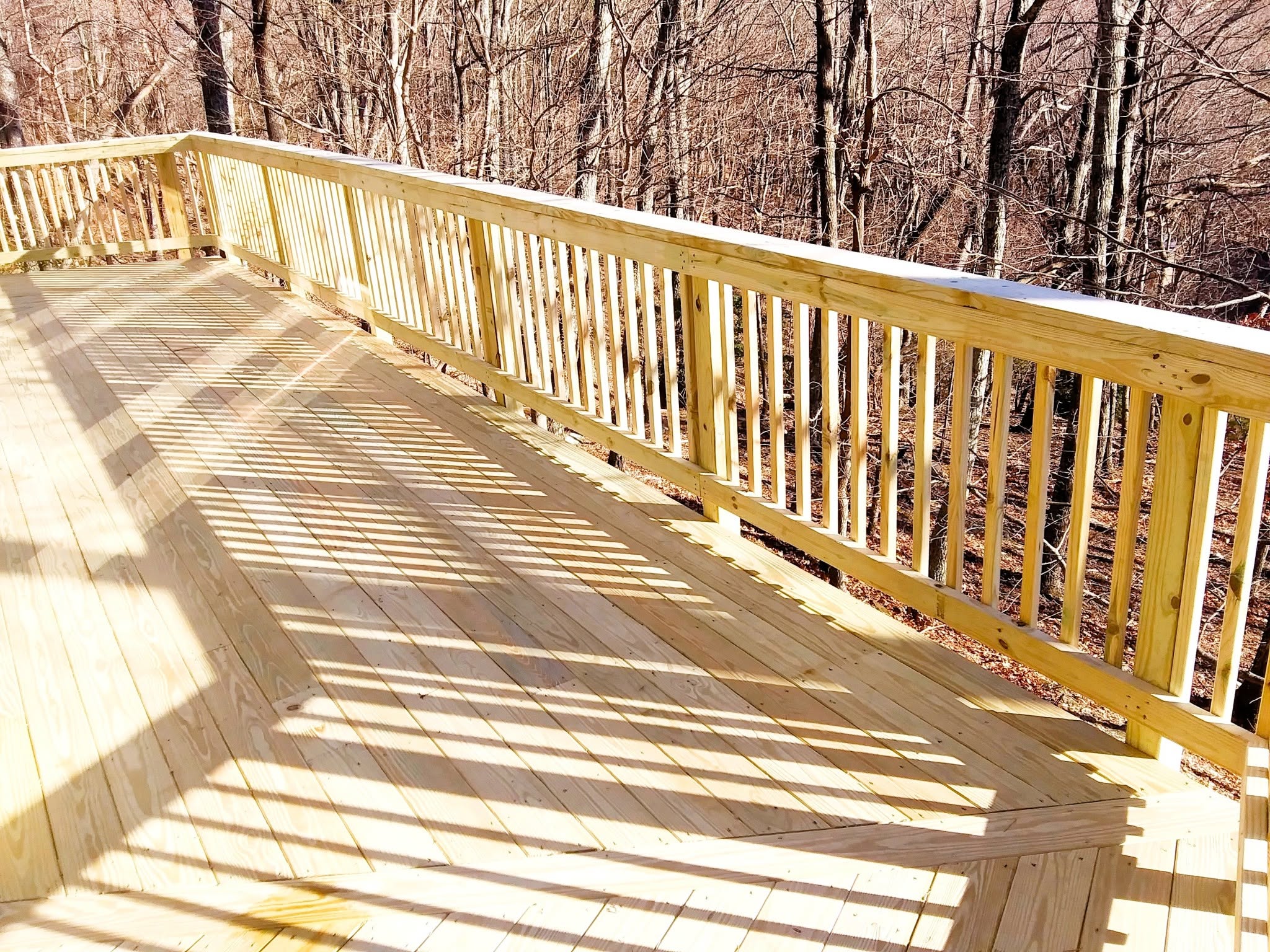 Freshly built pressure-treated deck with an angled bay corner and closely spaced wood baluster railing above winter woods