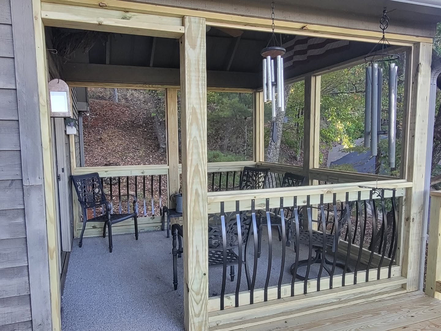 Screened porch with black aluminum balusters, gray composite floor and wind chimes facing the woods
