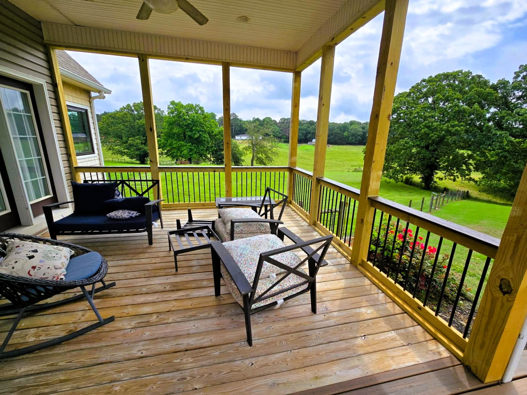 Screened porch with black baluster railing, beadboard ceiling and patio seating looking out over open pasture and oak trees