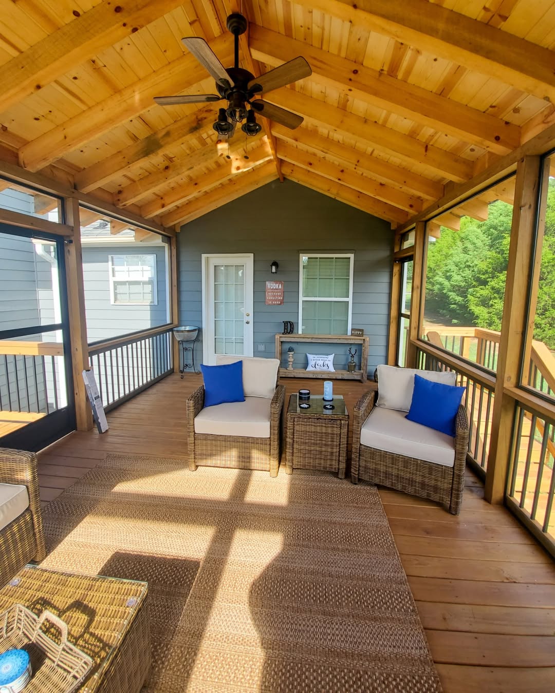 Screened porch with a cathedral pine ceiling, exposed rafters, ceiling fan and wicker seating on stained decking