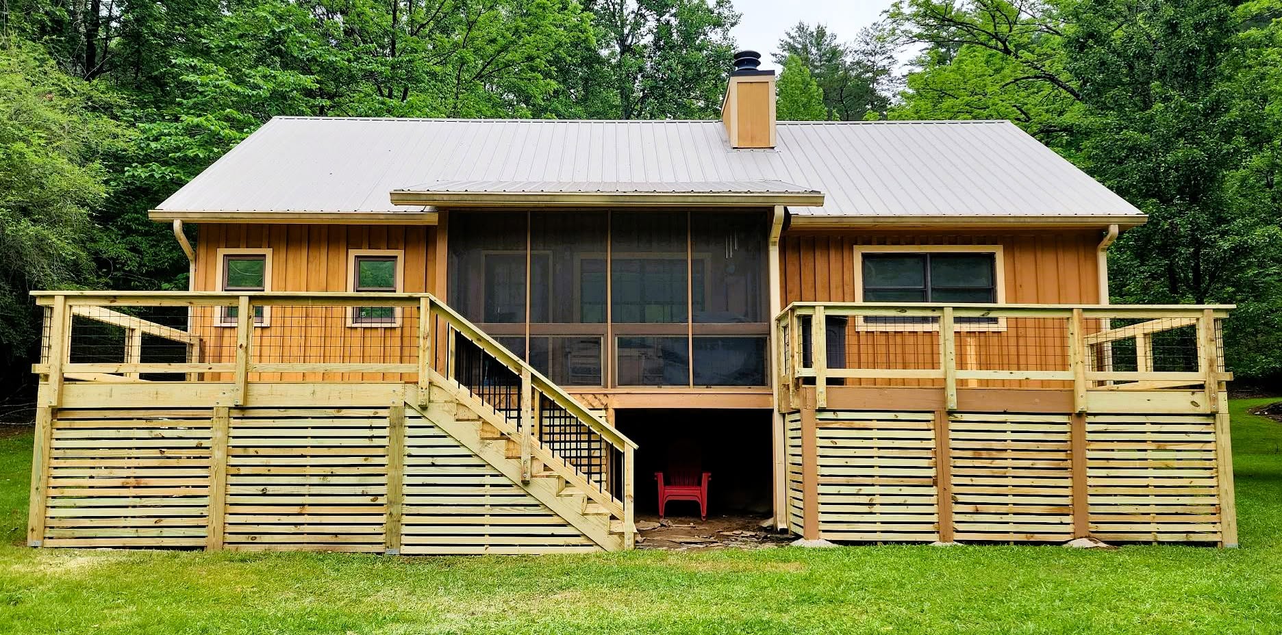 Central screened porch flanked by wire mesh deck railings, horizontal slat skirting below and a standing-seam metal roof above
