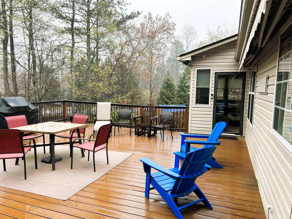 Large warm-stained wood deck with black aluminum railing and patio furniture beside a screened room on a rainy spring day