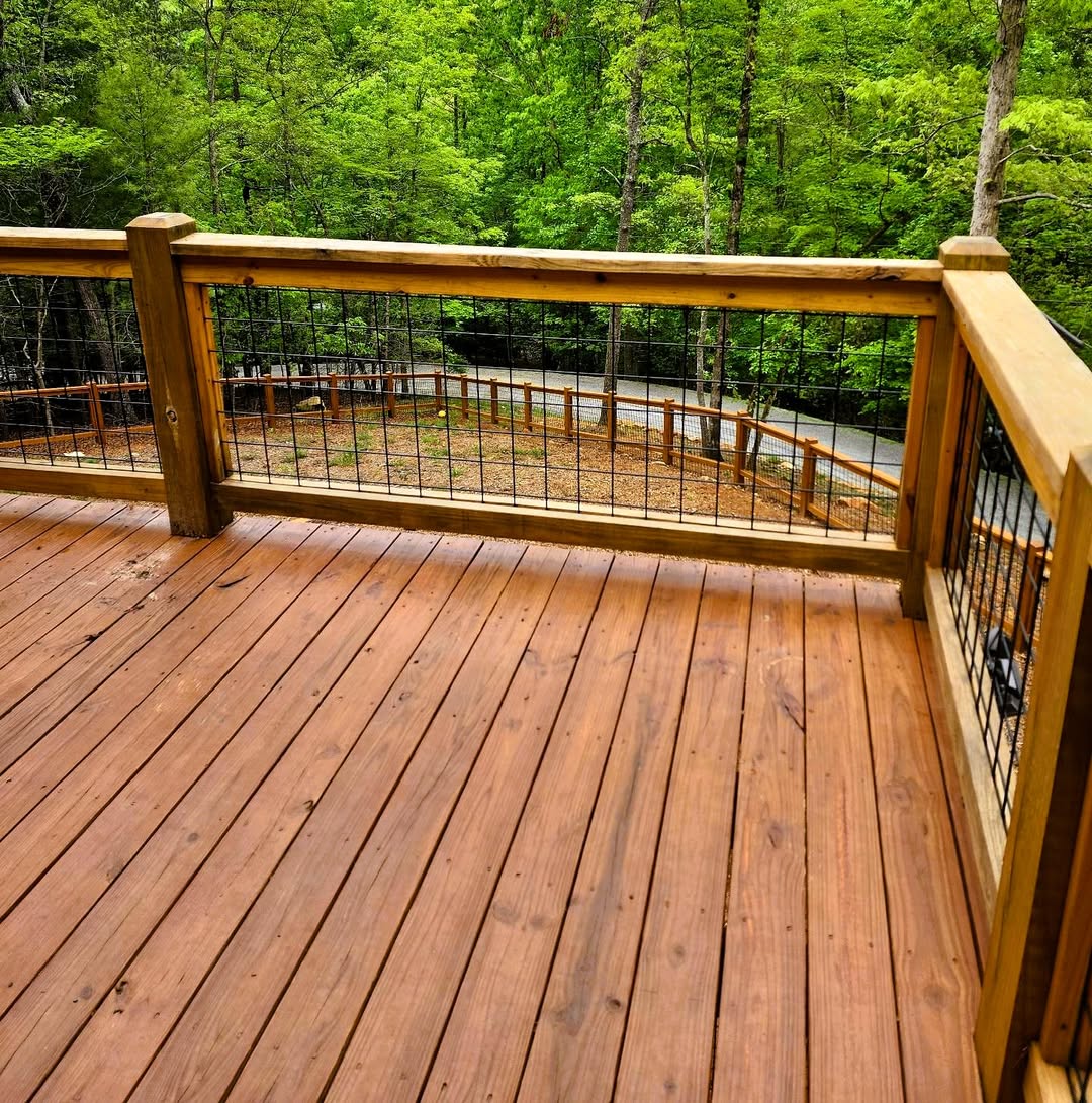 Warm stained wood deck bordered by wire mesh railing in heavy cedar frames overlooking a wooded drive