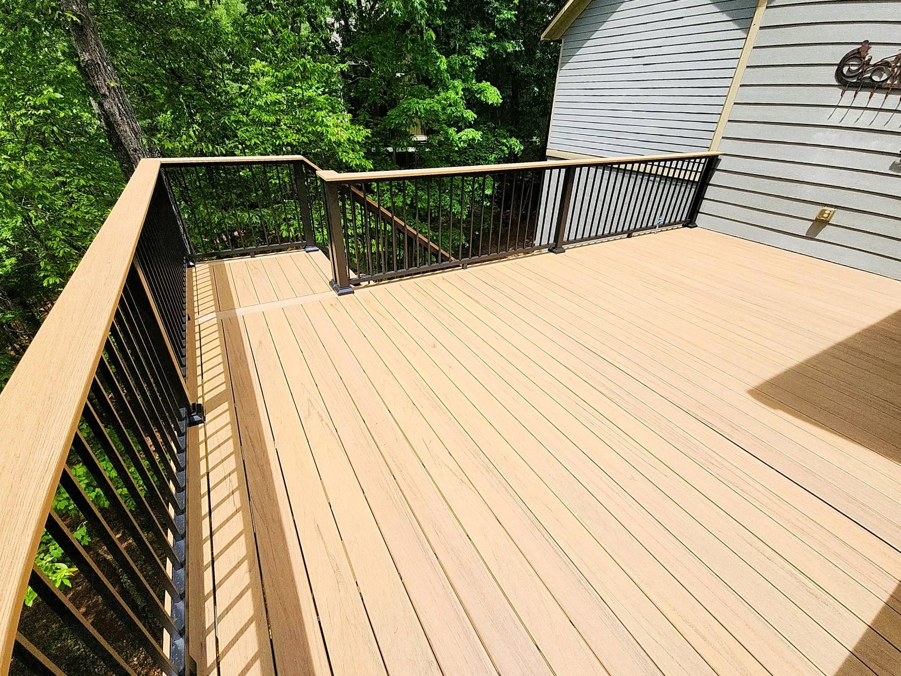 Two-level tan composite deck with black aluminum railing and matching composite top rail beside a gray-sided home