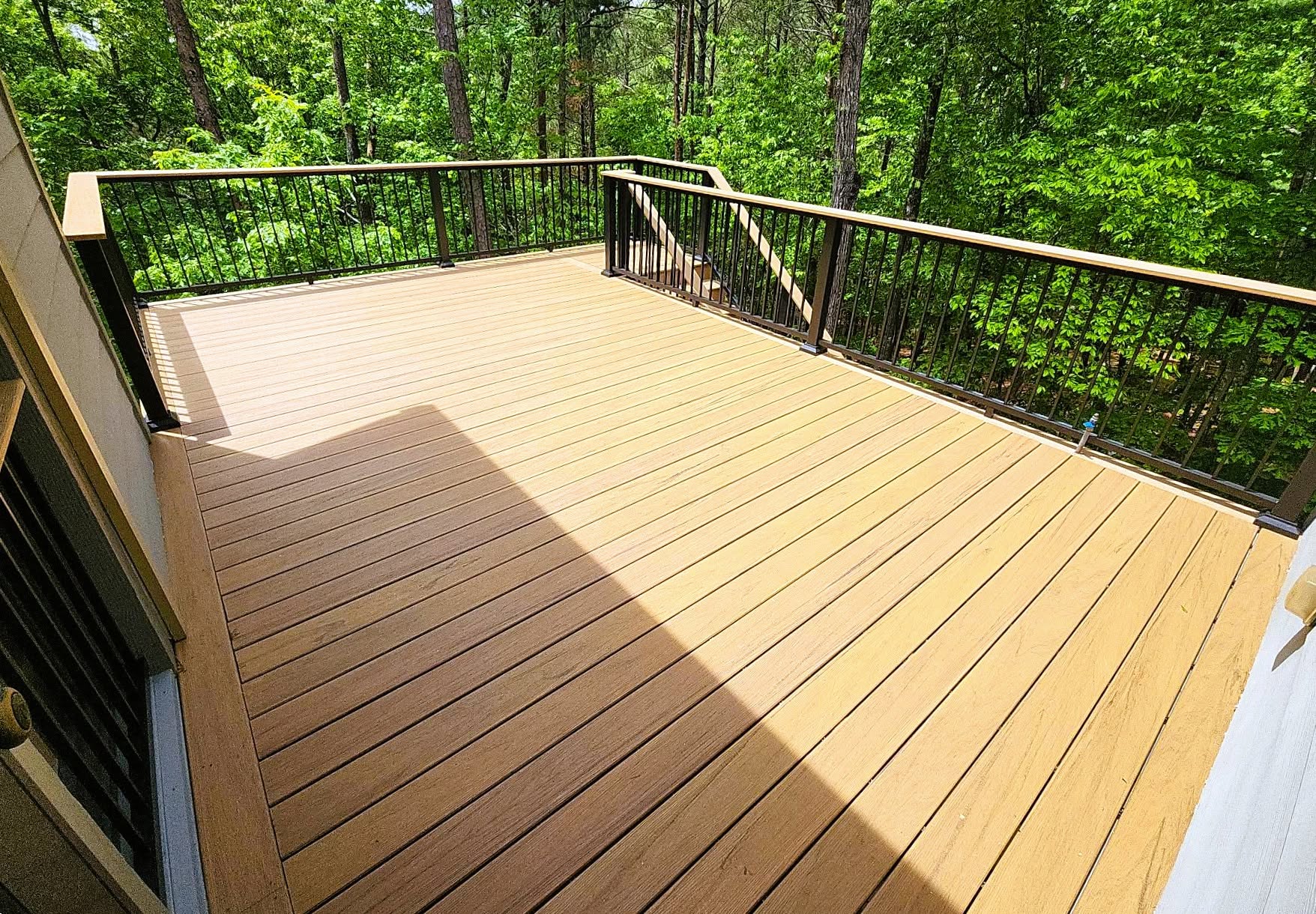 Golden-brown TimberTech Legacy composite deck with picture-frame border and black aluminum railing facing dense summer woods