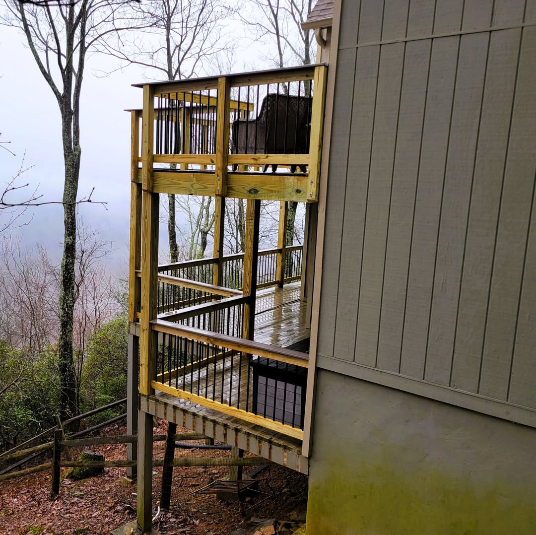 Two-story pressure-treated deck with black metal balusters stacked against a hillside home in mountain fog