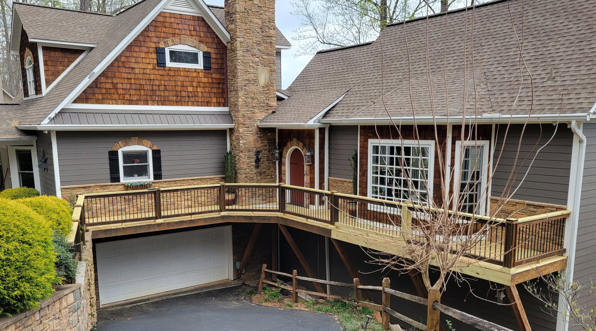 Wrap-around pressure-treated deck with black balusters curving around a cedar-shingled home with a stone chimney